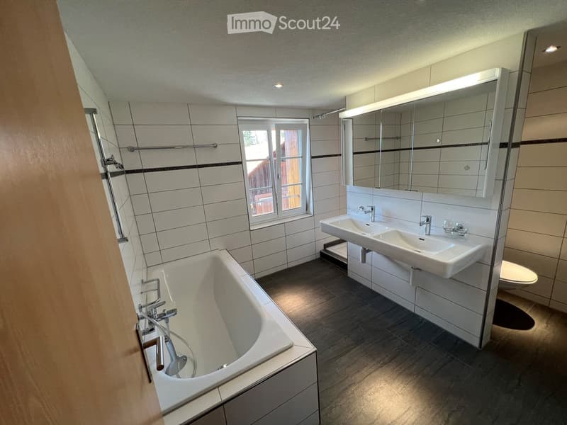 Bathroom with bathtub, double sink, toilet, and mirror