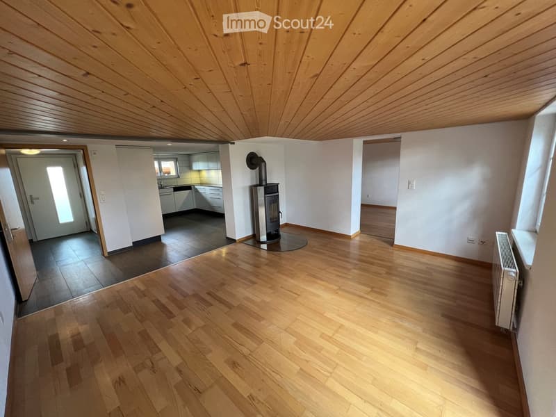 empty room, wooden floor, white walls, wooden ceiling, fireplace, kitchen in the background