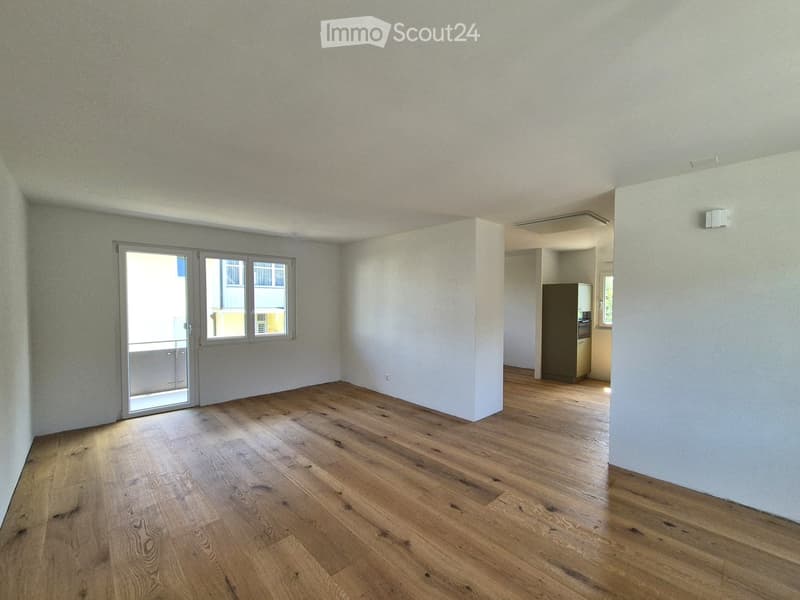 Empty room with wooden flooring, white walls, and a sliding glass door leading to a balcony.