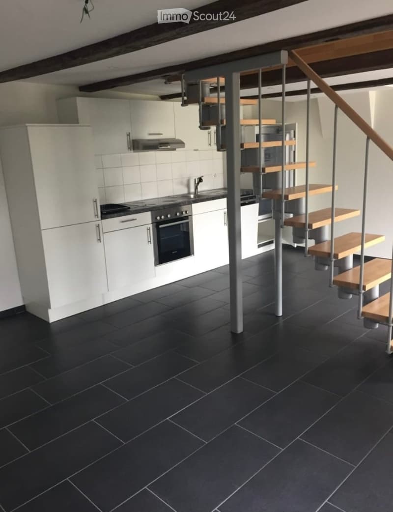 Modern kitchen with white cabinets, black tiled floor, stainless steel appliances, and a staircase leading to an upper level.