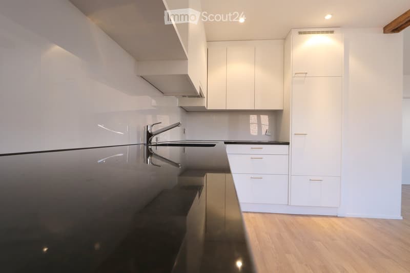 Modern kitchen with white cabinets, a sleek black countertop, and a stainless steel faucet.