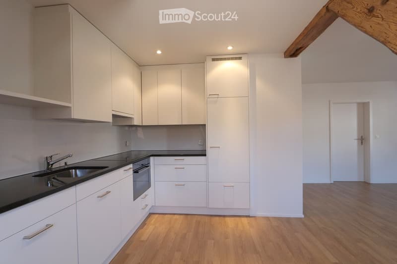 Modern kitchen with white cabinets, black countertops, a sink, and an oven. The floor is wooden, and the space is well-lit with recessed lighting.
