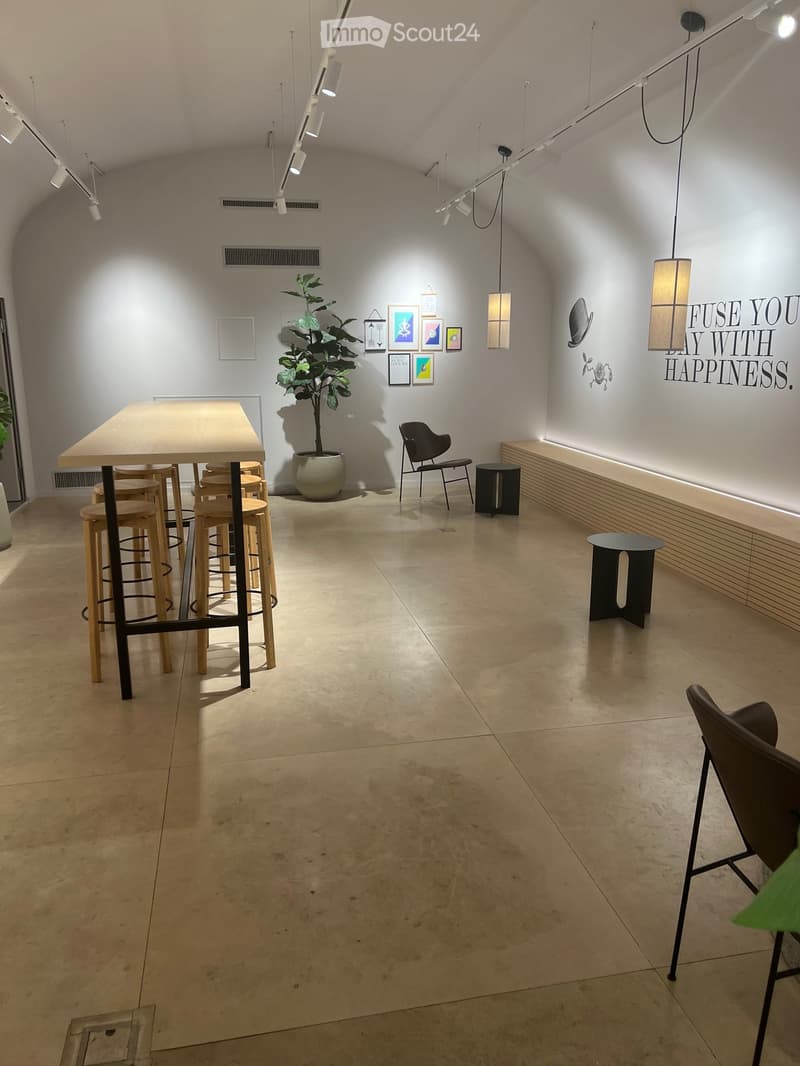 A room with a long table and stools, a chair, a bench, a potted plant, and a wall with a motivational quote.