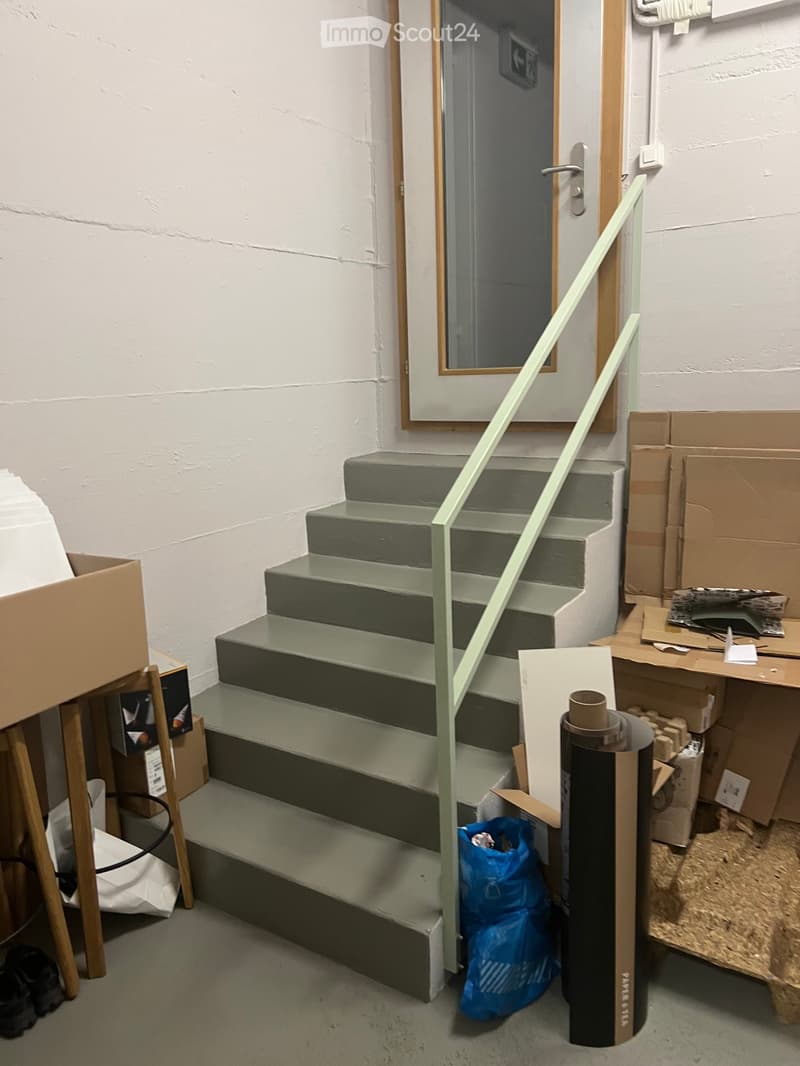 Concrete staircase with green handrail, leading to a door, surrounded by storage boxes and bags
