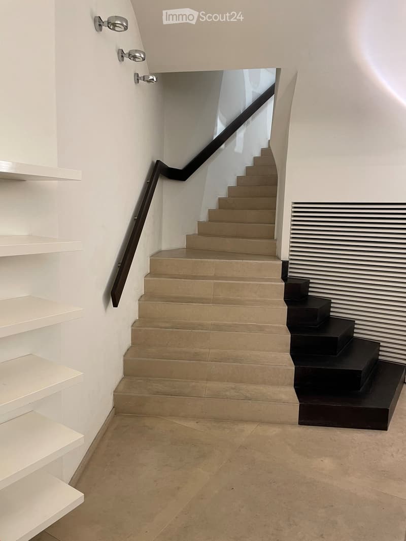 Modern staircase with beige and black steps, white walls, black handrail, white shelves