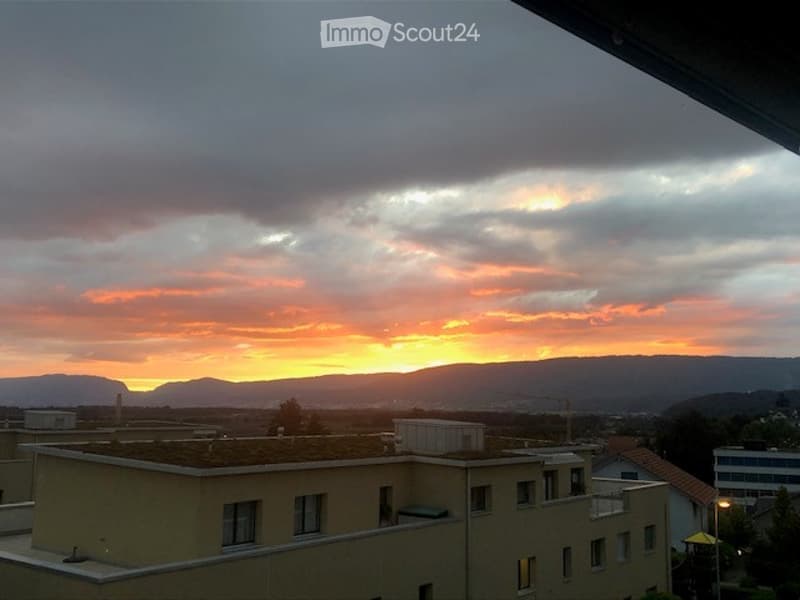 Balcony view overlooking a cityscape at sunset, with buildings and distant mountains visible.