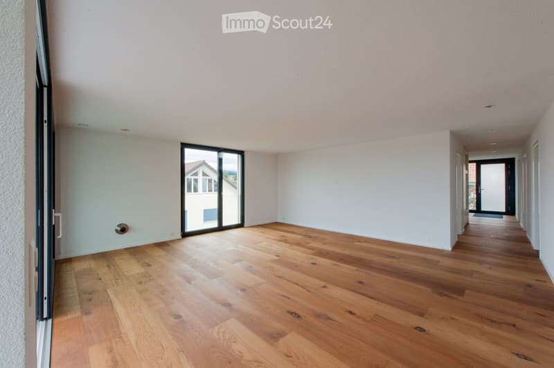 Empty hallway with wooden flooring, white walls, and large glass sliding doors leading to an outdoor area.