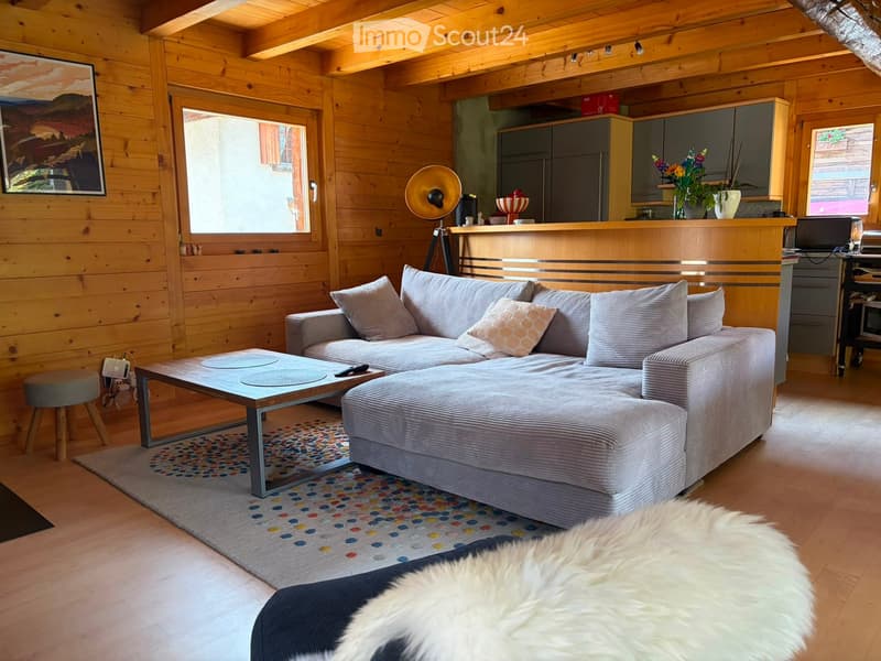 Cozy living room with wooden walls and ceiling, large sectional sofa, coffee table, floor lamp, and decorative vases.