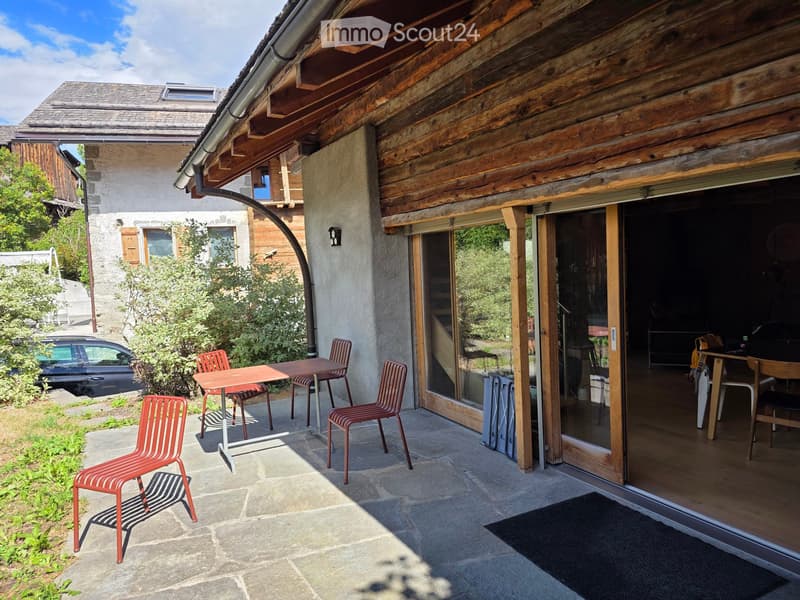 Outdoor patio with a wooden table and four red chairs, connected to a house with large glass doors.