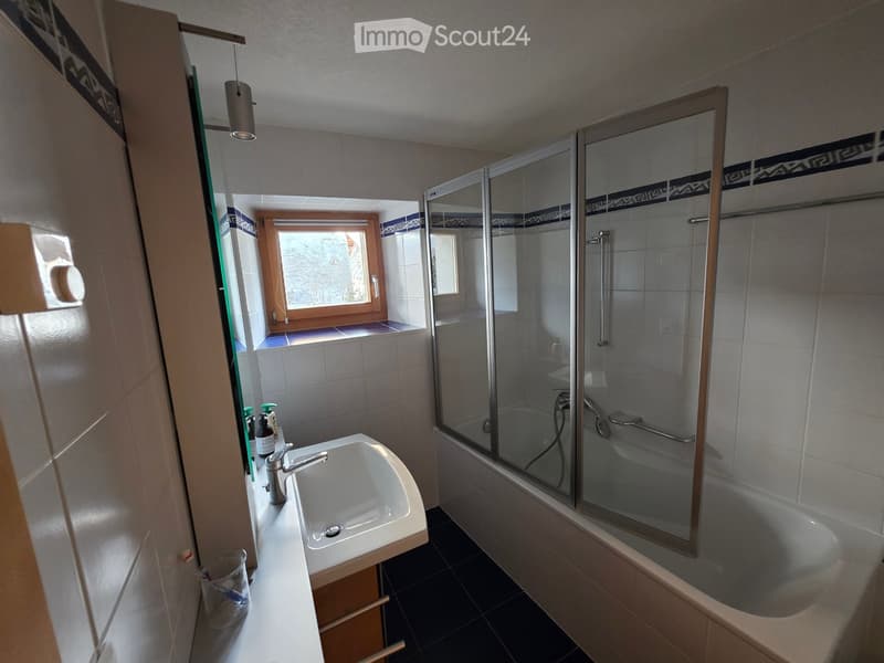 Bathroom with a white sink, bathtub with glass shower enclosure, and a window providing natural light.