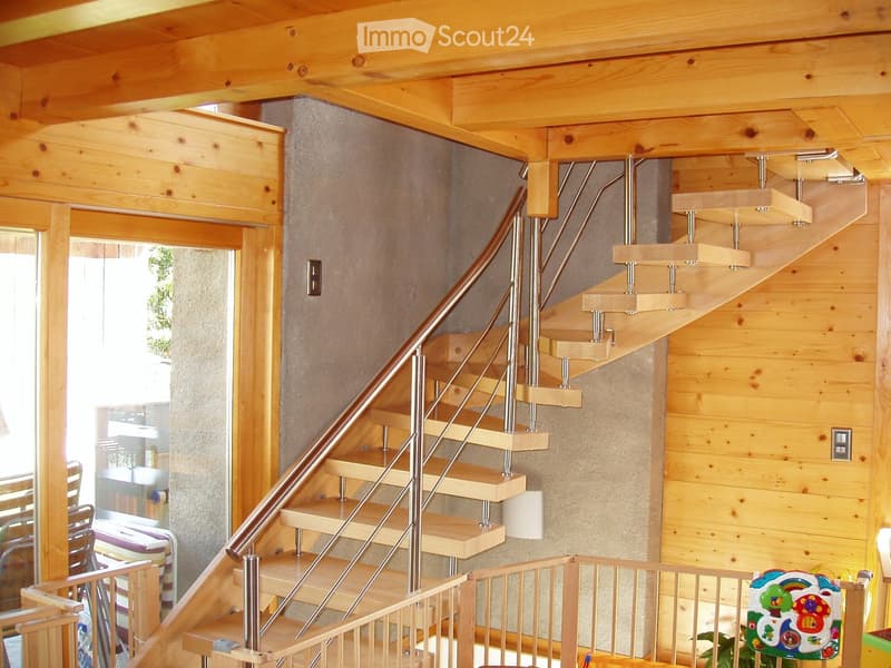 Spiral staircase with wooden steps and metal railings, leading to an open area with visible furniture and decor in the background.