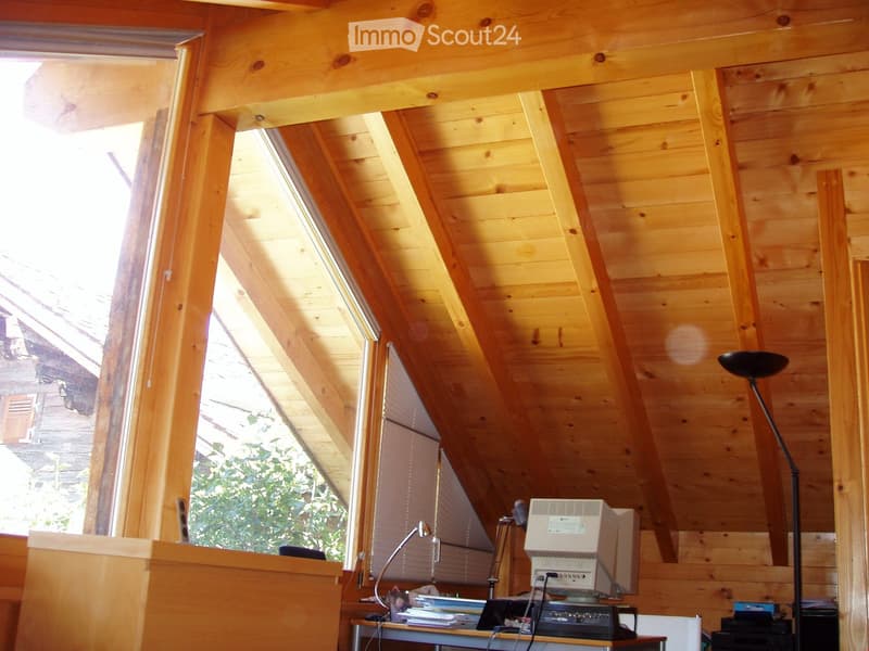 Wooden-paneled attic room with slanted ceilings, large windows, a desk with a computer, and a floor lamp.