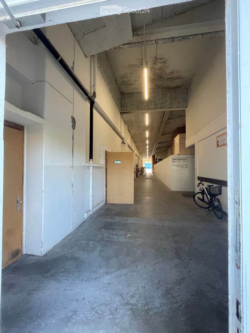 A long, narrow concrete corridor with white walls, a single overhead light, and a bicycle parked on the right side.