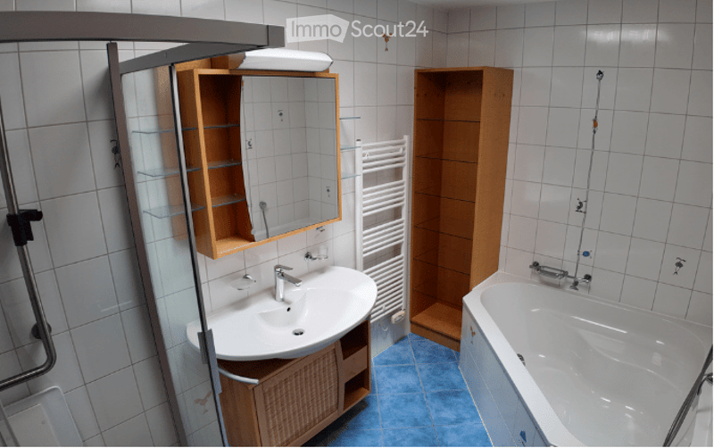 Modern bathroom with white tiles, a white sink, a mirror, a wooden cabinet, a bathtub, and a towel rack.