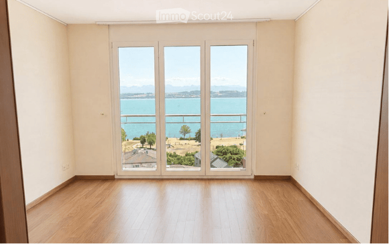 Empty room with wooden flooring and large glass doors opening to a balcony with a scenic sea view.