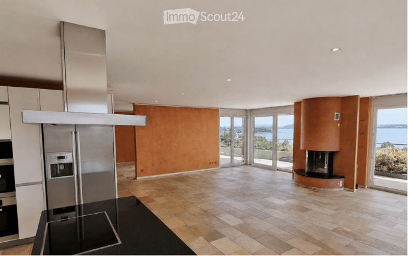 Modern, open-plan kitchen and living area with high ceilings, large windows offering a scenic view, stainless steel appliances, and a central island.