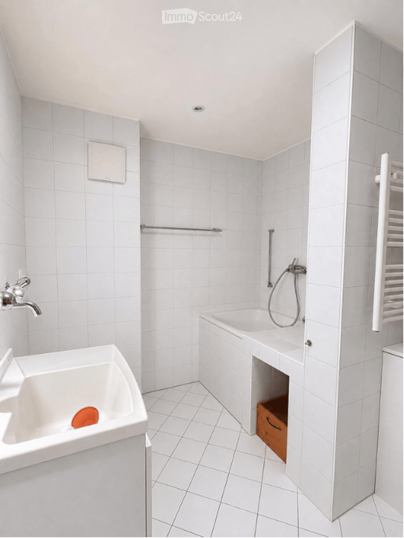 Modern bathroom with white tiled walls and floor, featuring a sink, bathtub, and showerhead.