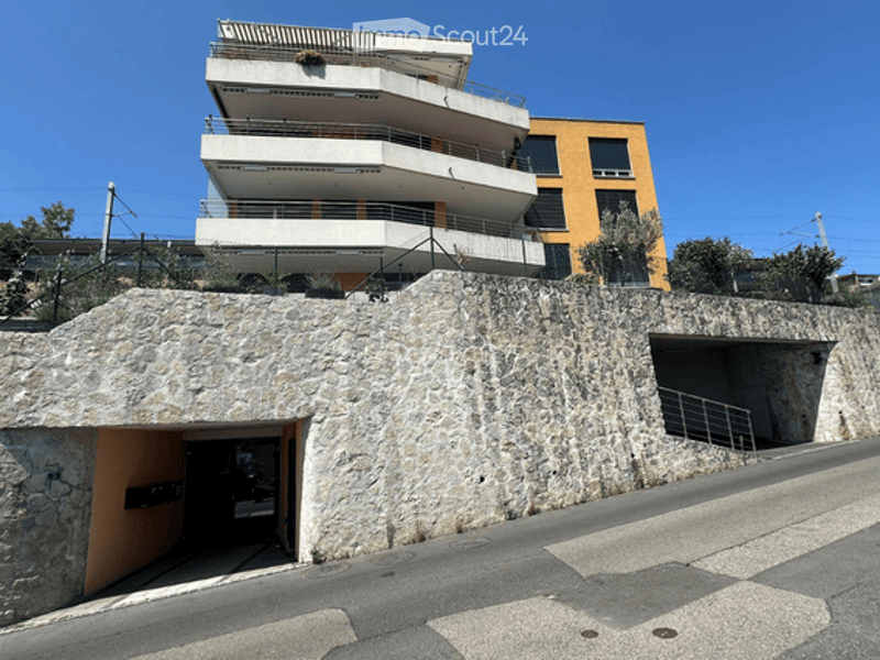 Modern multi-story apartment building with white balconies and a stone-covered garage entrance.