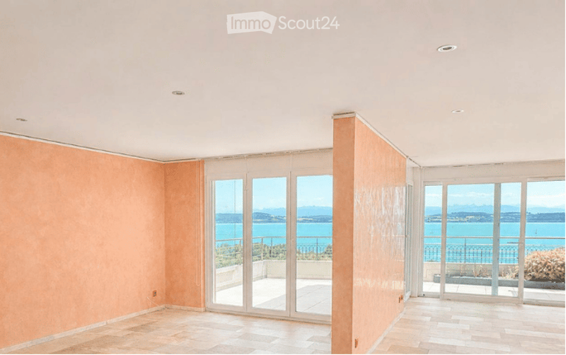 Empty room with peach-colored walls, large glass doors leading to a balcony with a scenic sea view.