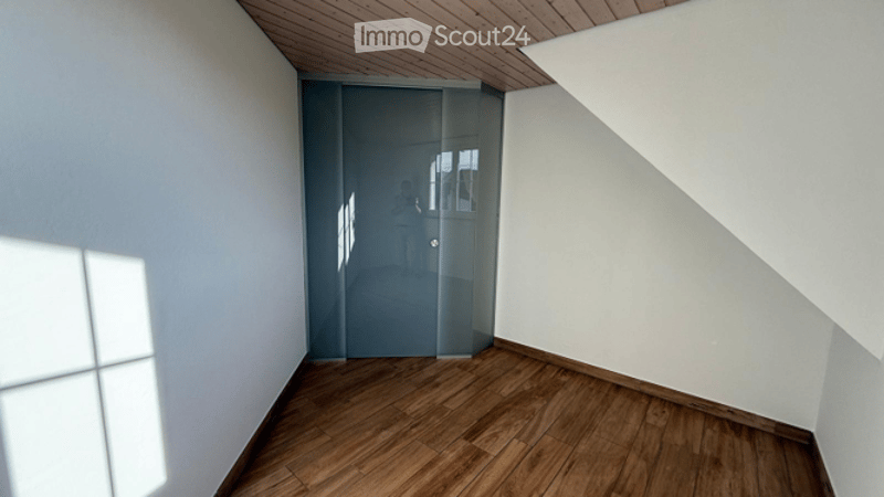 Empty room with wooden flooring, white walls, and a glass sliding door leading to another space.