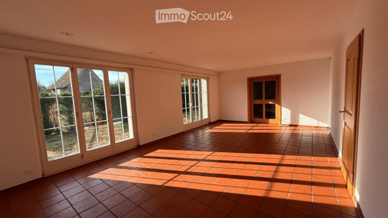 Empty room with tiled floor, large windows, and a wooden door. No furniture or equipment present.