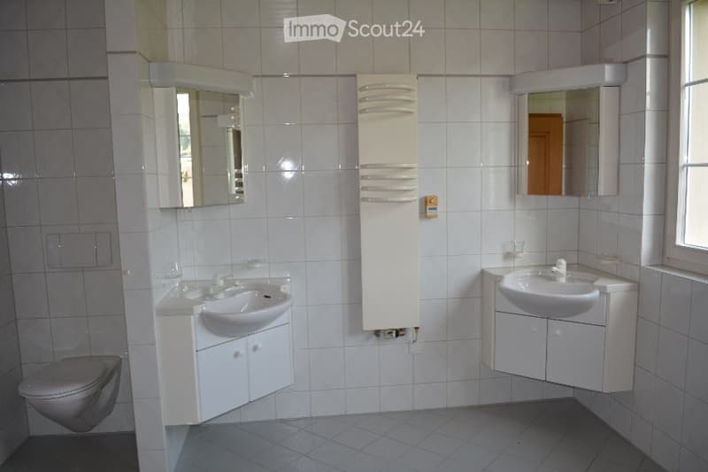 Modern bathroom with white tiles, two sinks, mirrors, and a toilet.