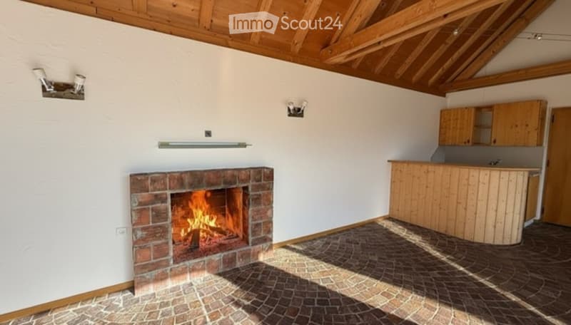 Cozy room with exposed wooden beams, brick fireplace, kitchen counter, and wooden cabinets.