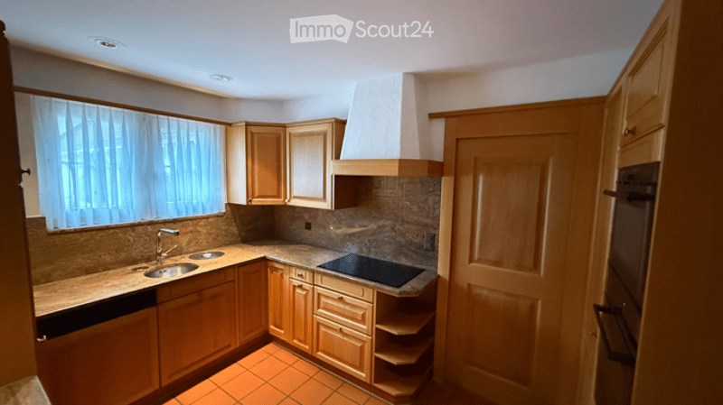 A modern kitchen with wooden cabinets, granite countertops, a stainless steel sink, a dishwasher, and a built-in stove with a range hood. The space features a window with white curtains and a tiled floor.