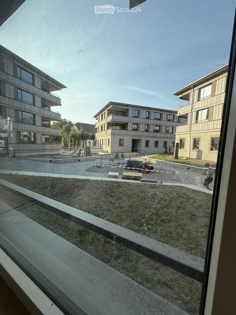 View from a window showing a residential complex with modern buildings, playground, and construction area.