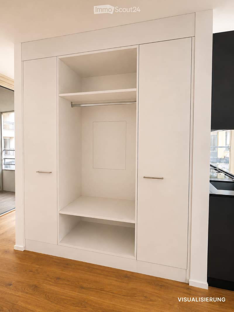 Empty room with white built-in closet featuring shelves and a hanging rod, wooden floor, and a glimpse of a kitchen area with black appliances.
