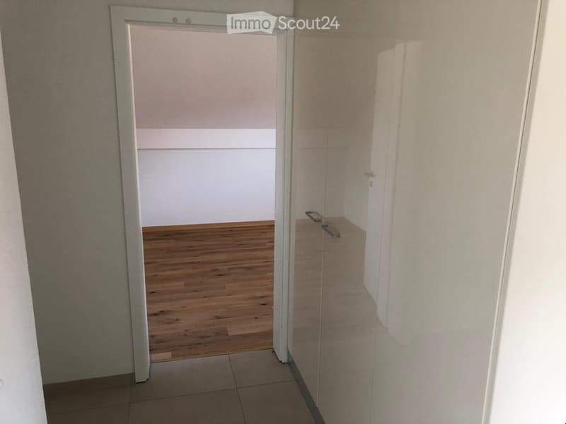 Empty hallway with wooden flooring and white walls, featuring a door leading to another room.