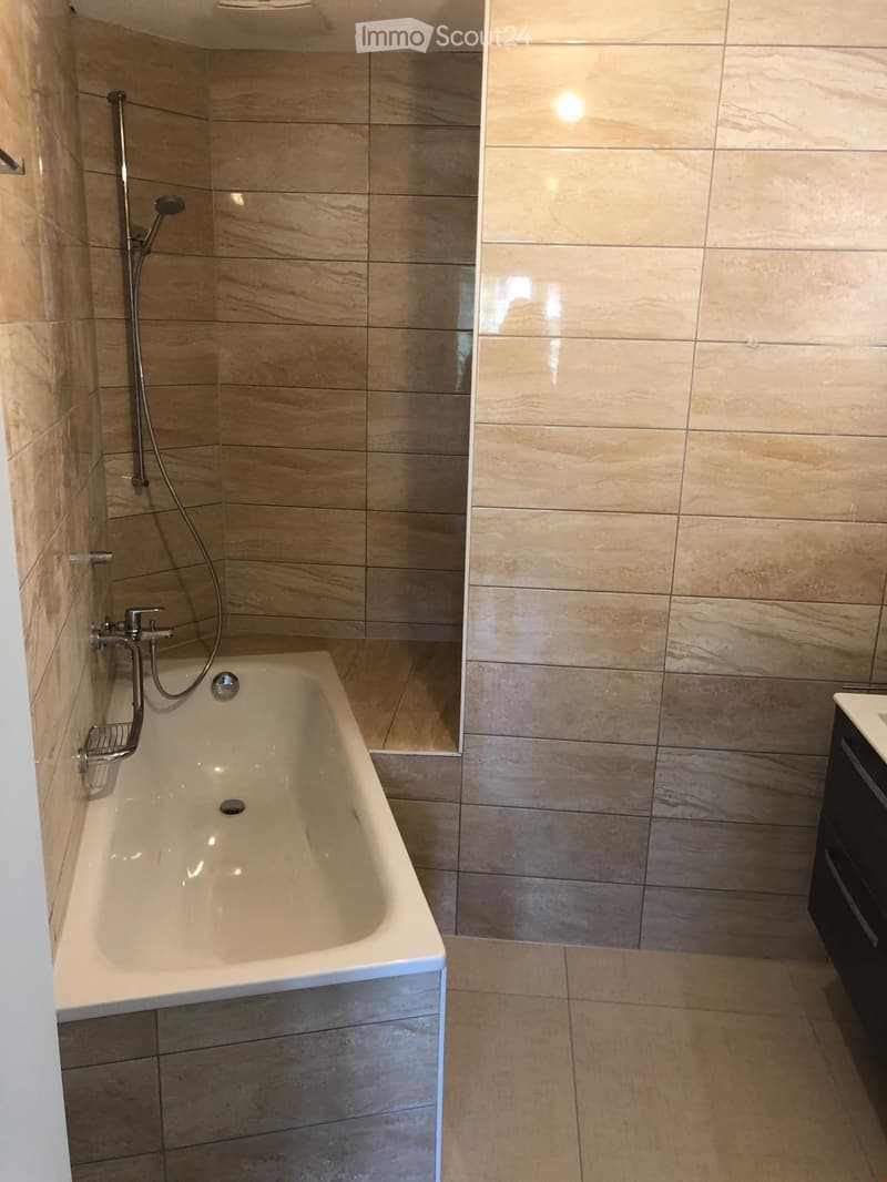 Modern bathroom with a bathtub, tiled walls, and a showerhead attached to the wall.