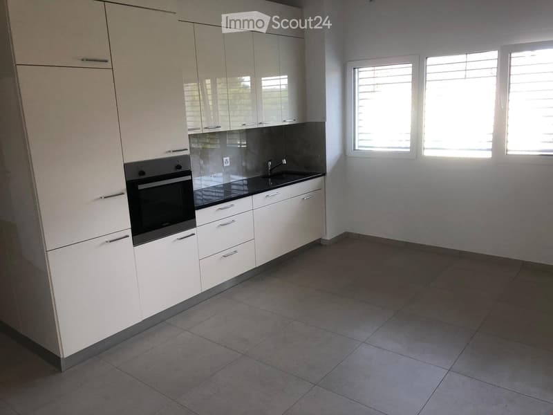 Modern kitchen with white cabinets, black countertop, built-in oven, and three windows with blinds.