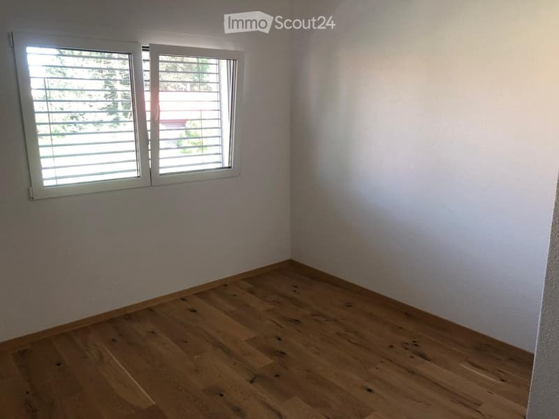 Empty room with wooden flooring and white walls, featuring two windows with white frames and blinds.