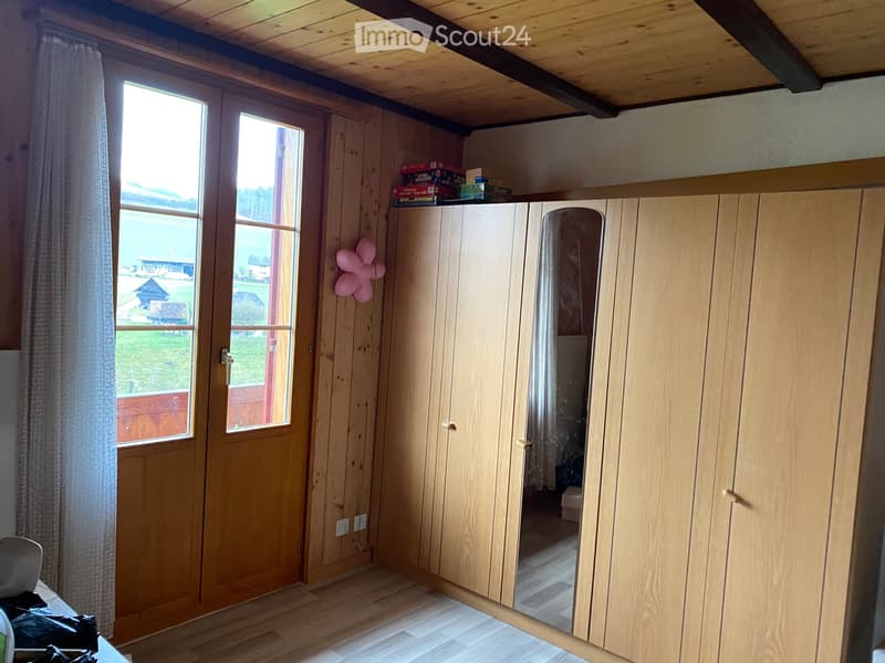 Empty room with wooden walls, wooden floor, large window with view of outdoor area, wooden wardrobe, and a pink balloon decoration on the wall.