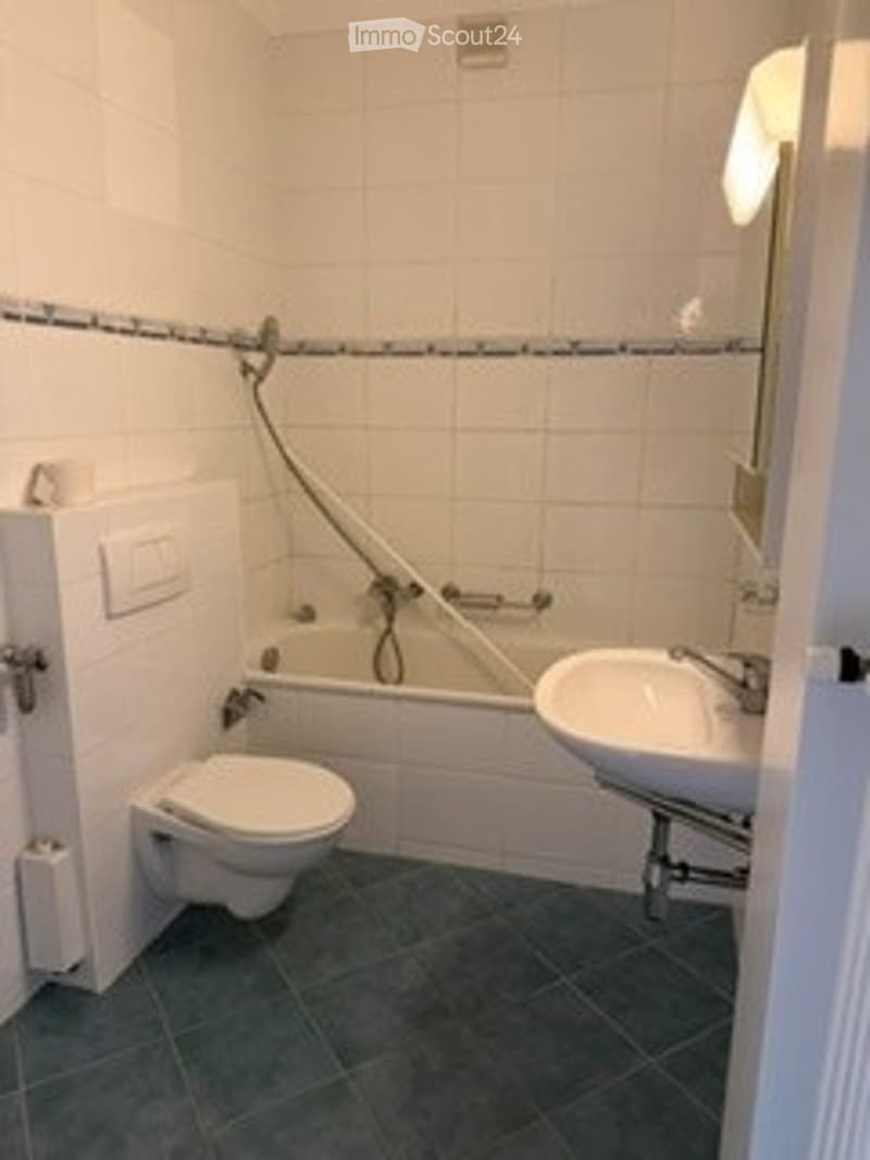 A small bathroom with white tiled walls and floor, featuring a toilet, bathtub, and sink with a mirror above it.