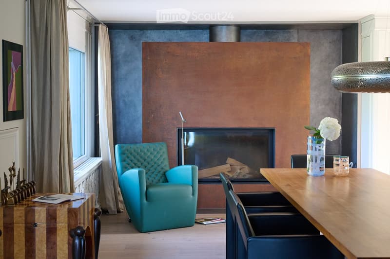 Modern living room with a fireplace, teal sofa, wooden table, and decorative vase.