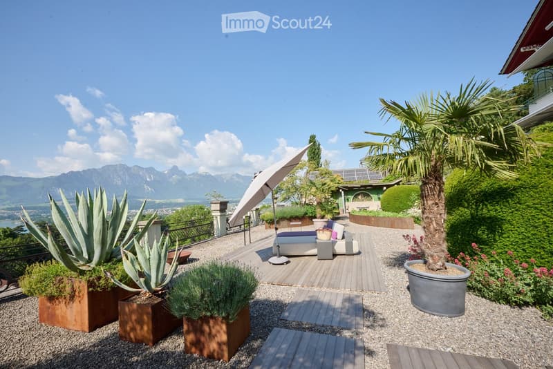 A spacious outdoor terrace with a modern seating area, large potted plants, and a scenic mountain view.