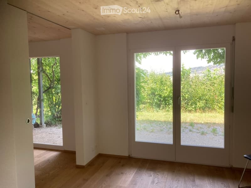 Empty room with wooden flooring, large sliding glass doors, and a view of greenery outside.