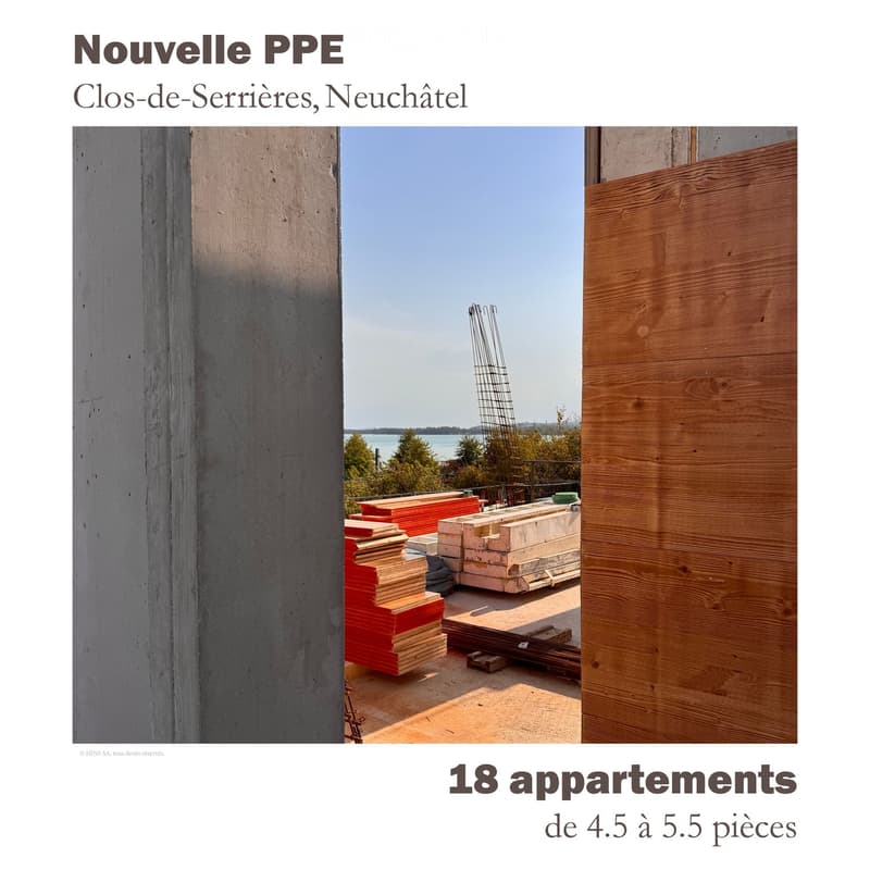 Construction site with stacks of wooden planks, concrete blocks, and metal scaffolding, with a view of the lake and distant trees.