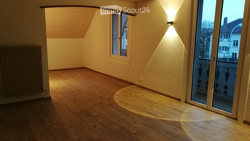 Empty room with wooden floor, glass doors leading to a balcony, white walls, mounted radiator, wall lamp, and windows