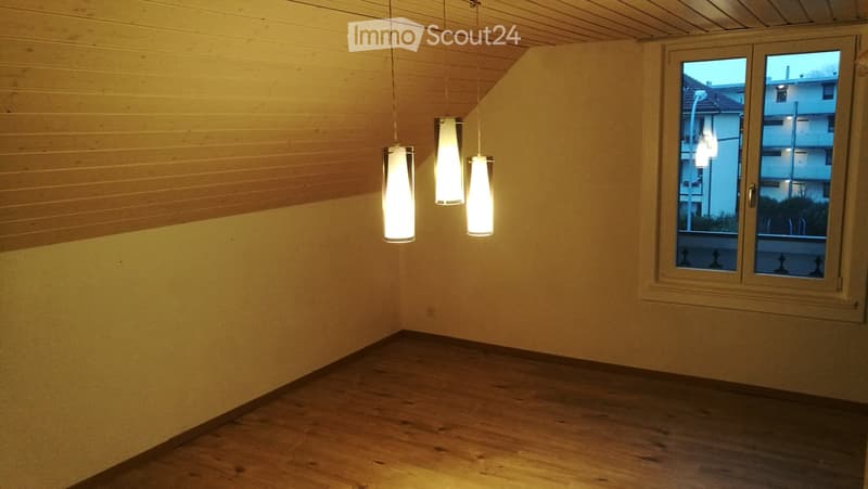 large empty room with white walls, wooden floor, wooden beams on the ceiling, hanging lights, windows