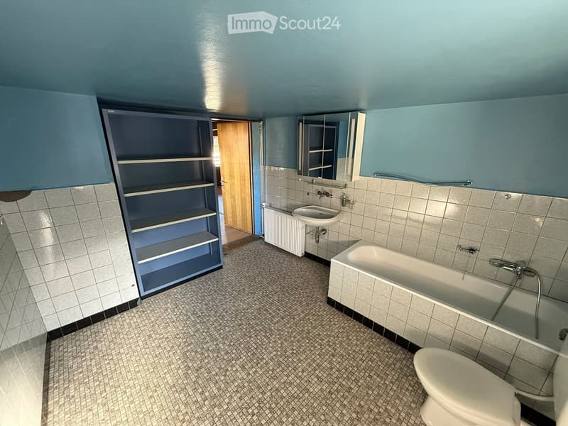 Bathroom with blue walls, tiled floor, bathtub, sink, toilet, mirror, radiator, and cabinet.