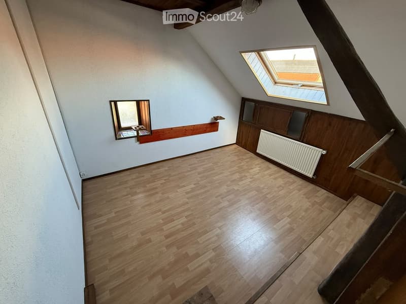 Empty attic room with wooden flooring, white walls, and a skylight window. There is a radiator and a small mirror on the wall.