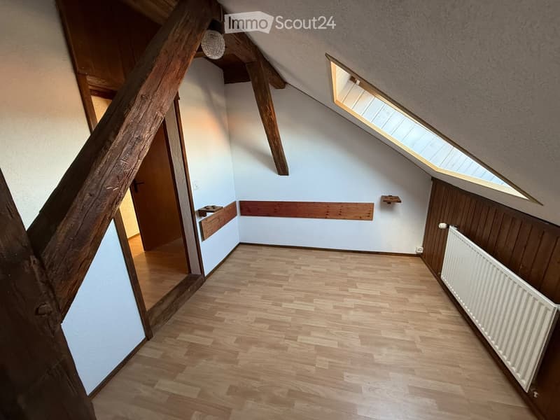 Empty attic space with wooden floors, exposed wooden beams, skylight windows, and a radiator on one wall.