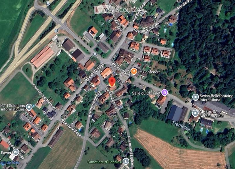 Aerial view of a small village with houses, roads, and green spaces.