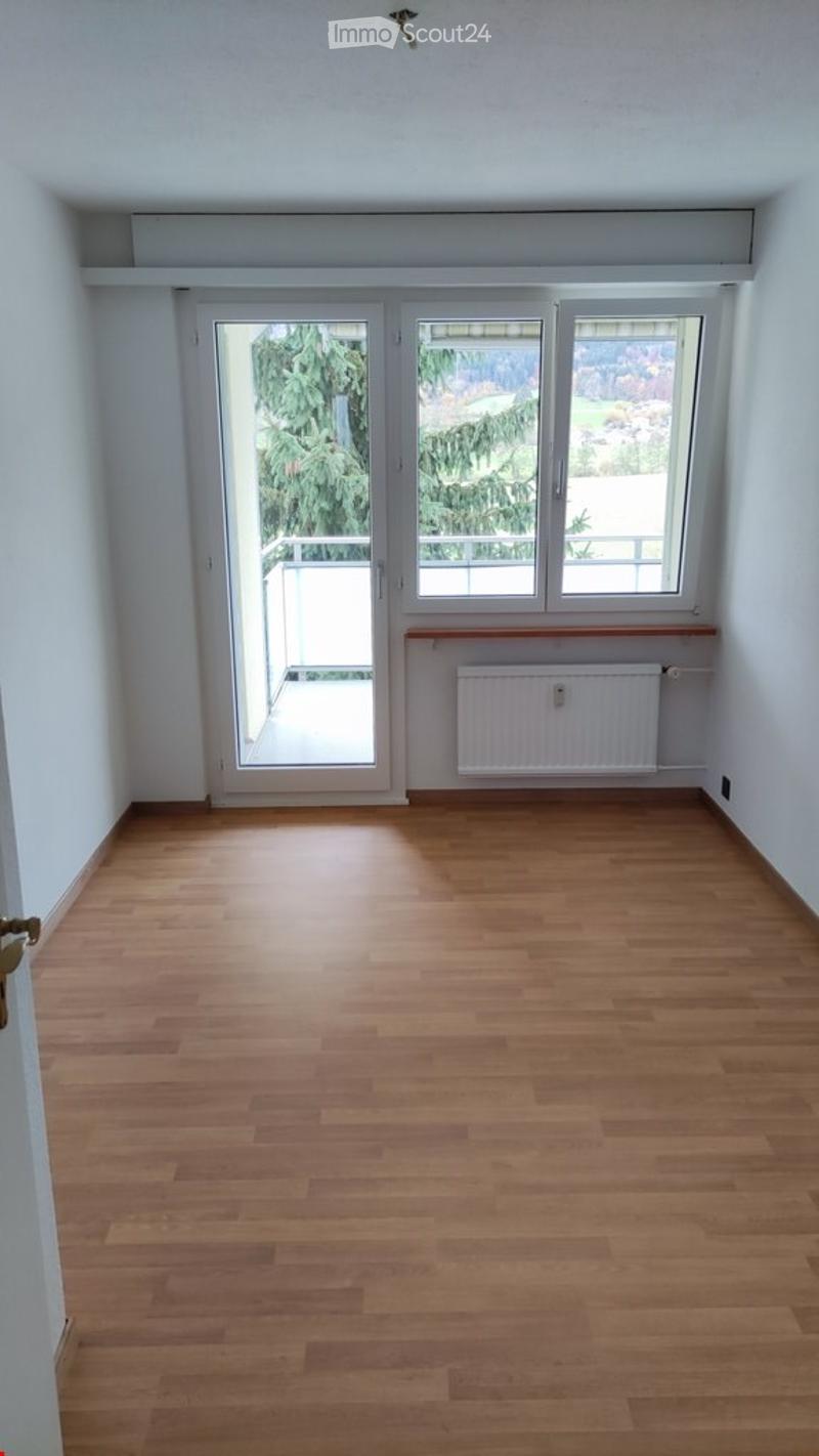 Empty room with wooden flooring, white walls, large windows, and a sliding glass door leading to a balcony.