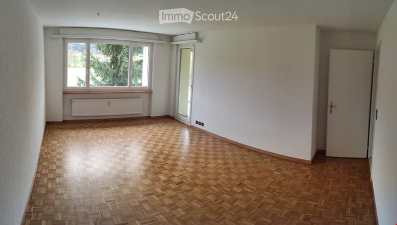 Empty room with wooden parquet flooring, white walls, large windows, and a radiator. No furniture or equipment present.