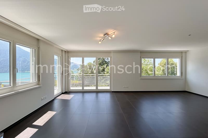 Empty room with dark tiled flooring, large windows, and sliding glass doors leading to a balcony. The walls are light-colored, and the ceiling has recessed lighting.