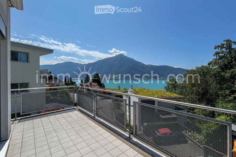 Balcony with tiled floor and metal railing, overlooking a scenic lake and mountain landscape.